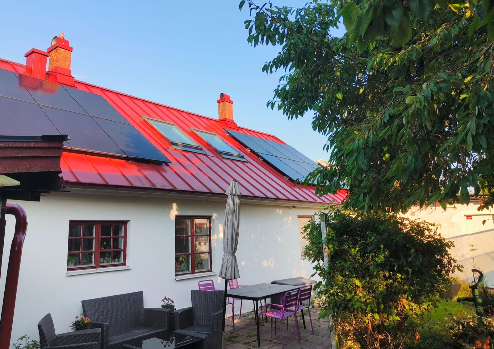 Solceller på rött falsat plåttak på vitt hus i Balkåkra i kvällssol